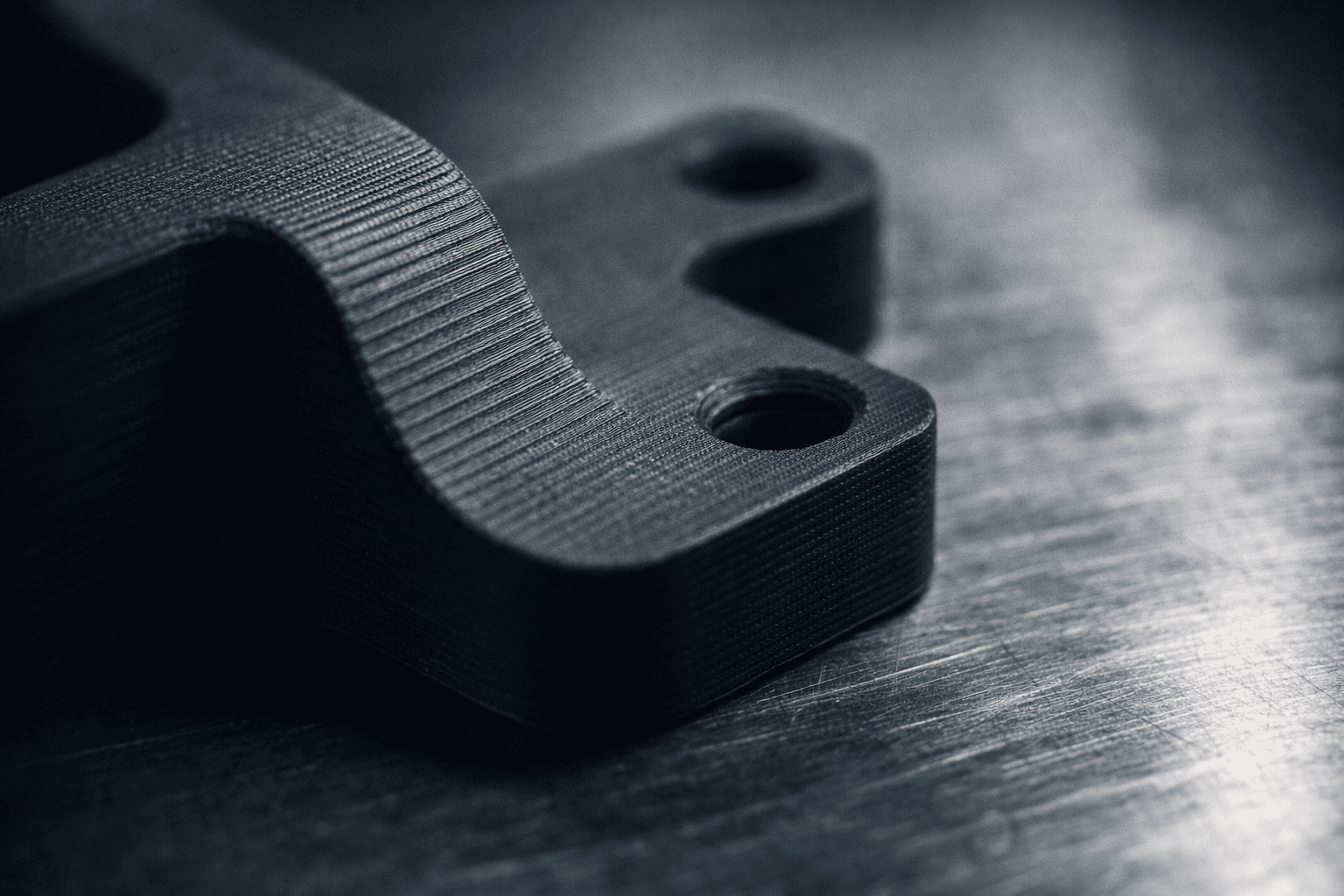 Macro close-up of a 3D printed carbon fiber bracket showing precise FDM layer lines