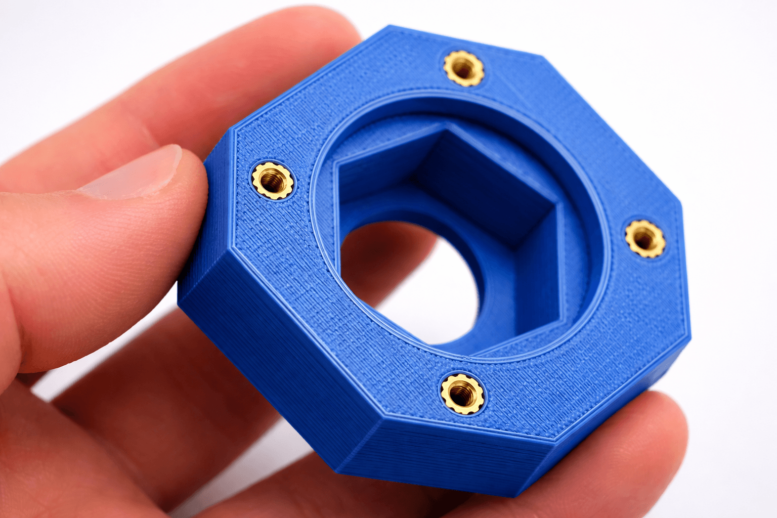Blue octagonal 3D printed part with seven heat-set brass threaded inserts installed — a finishing service performed in-house at TAKT 3D
