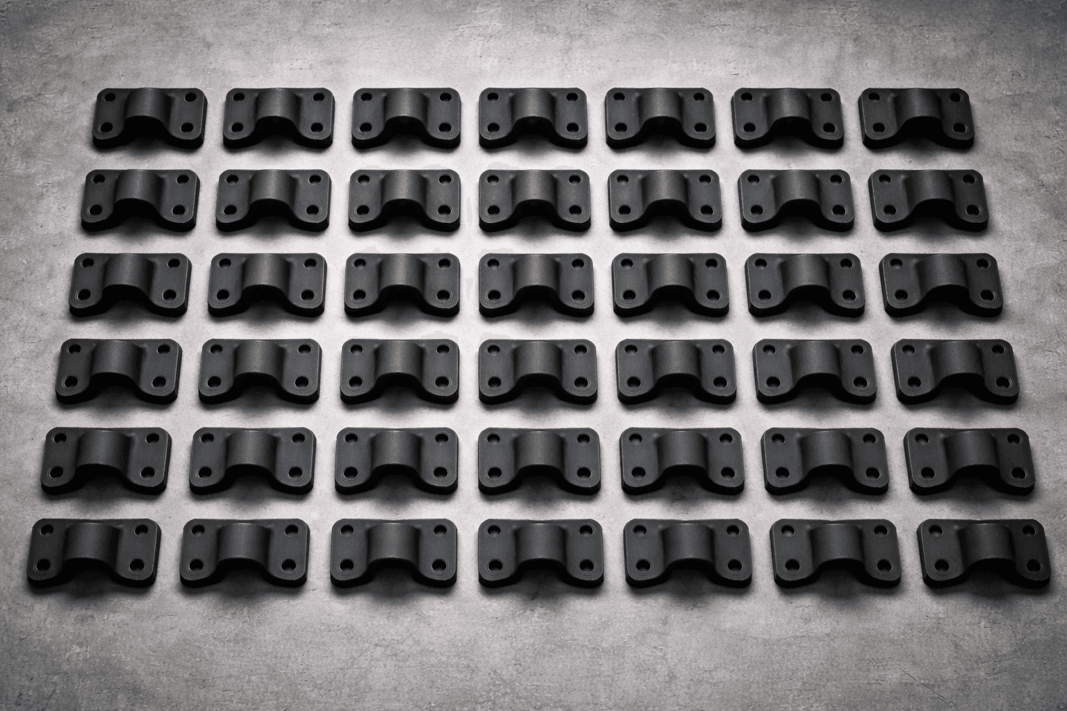 Grid of identical 3D printed black carbon-fiber production brackets arranged in rows